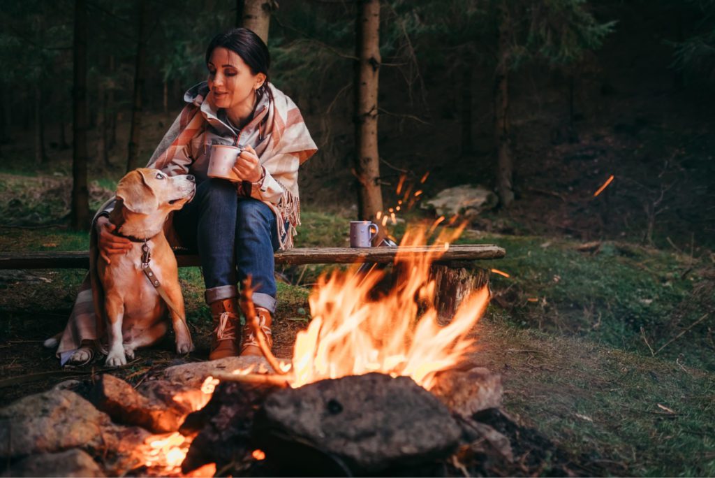 woman and dog drinking coffee by fire
