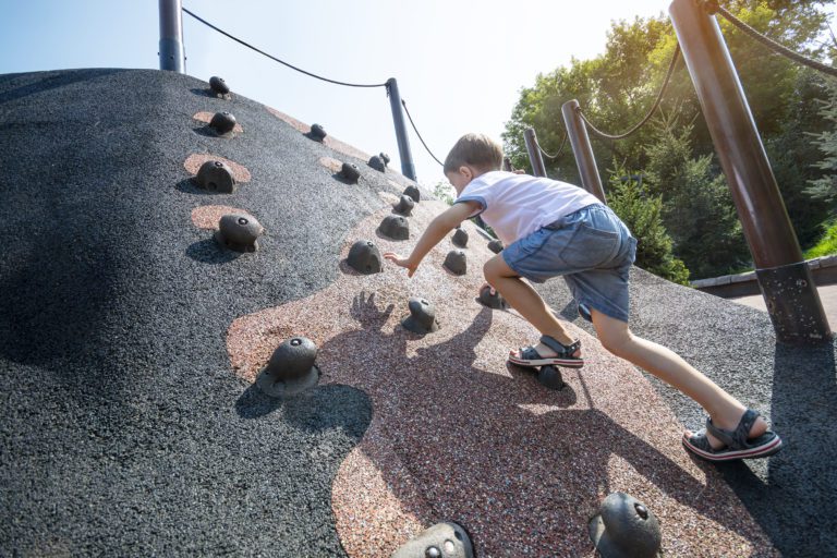 Little boy climbs to the training artificial mountain for the children at the municipal playground.